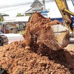 an excavator digging up a pile of fill dirt that will be transported to a comercial construction site to begin building a project foundation