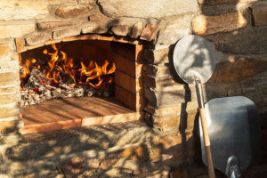 an outdoor pizza oven burning wood with a pizza peel next to it