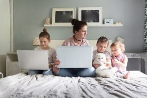 Mom and her three children are sitting on bed with laptops in their newly added home addition