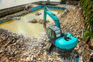 Swimming pool being demolished by Backhoe. A full pool removal is a more expensive method