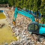 swimming pool being demolished by backhoe for rebuilding