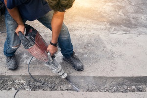 worker repairing driveway surface with jackhammer