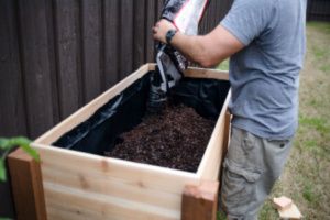 A man is filling a raised garden bed with soil