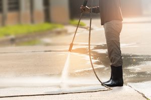 A man, power washing a concrete driveway on a sunny day