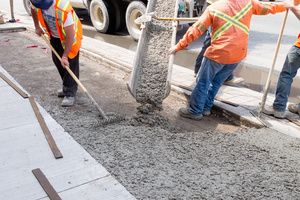 Two workers managing the flow of a vehicle pouring concrete on a driveway