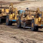 earthmoving equipment including scapers and motor graders involved in grading operations at a construction site